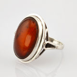 Silberner Ring mit großem ovalem Bernstein in Orange-Braun auf weißem Hintergrund