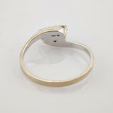 Silberner Ring mit ovalem Besatz und kleinen Perlen auf weißer reflektierender Fläche.
