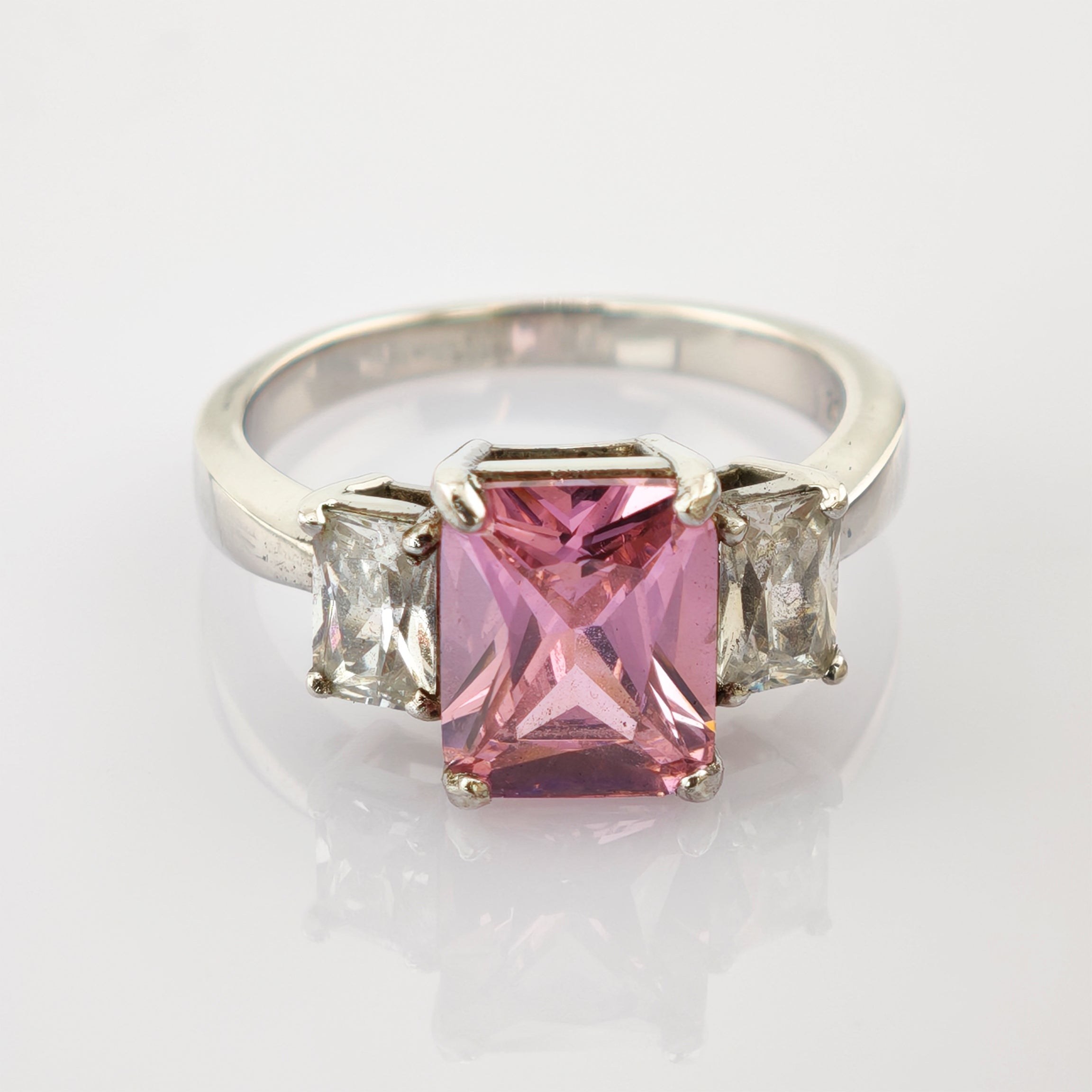 Silberner Ring mit rechteckigem rosa Edelstein und klaren Steinen auf glattem Band.
