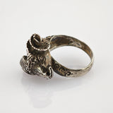 Silberner Ring mit Scheibenkopfmotiv und Hörnern auf hellem, grauem Hintergrund.