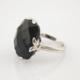 Silberner Ring mit großem, facettiertem schwarzen Edelstein und vier blattförmigen Krappen.