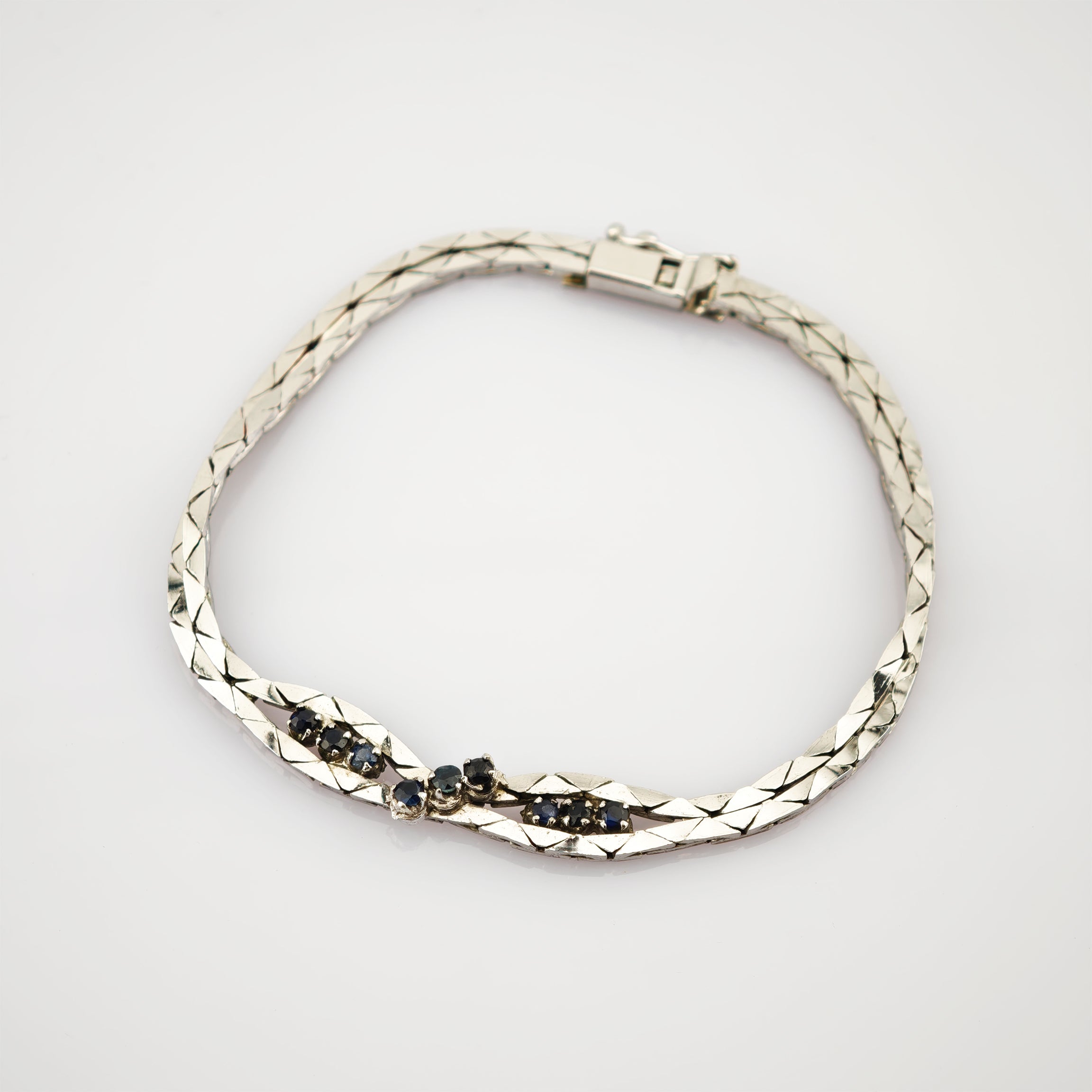 Silbernes Armband mit Diamantmuster und kleinen dunklen Edelsteinen in zwei mittleren Abschnitten.
