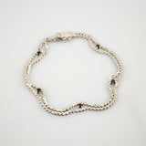 Silbernes Armband mit doppelter Kettenoptik und kleinen schwarzen runden Edelsteinen auf weißem Hintergrund.