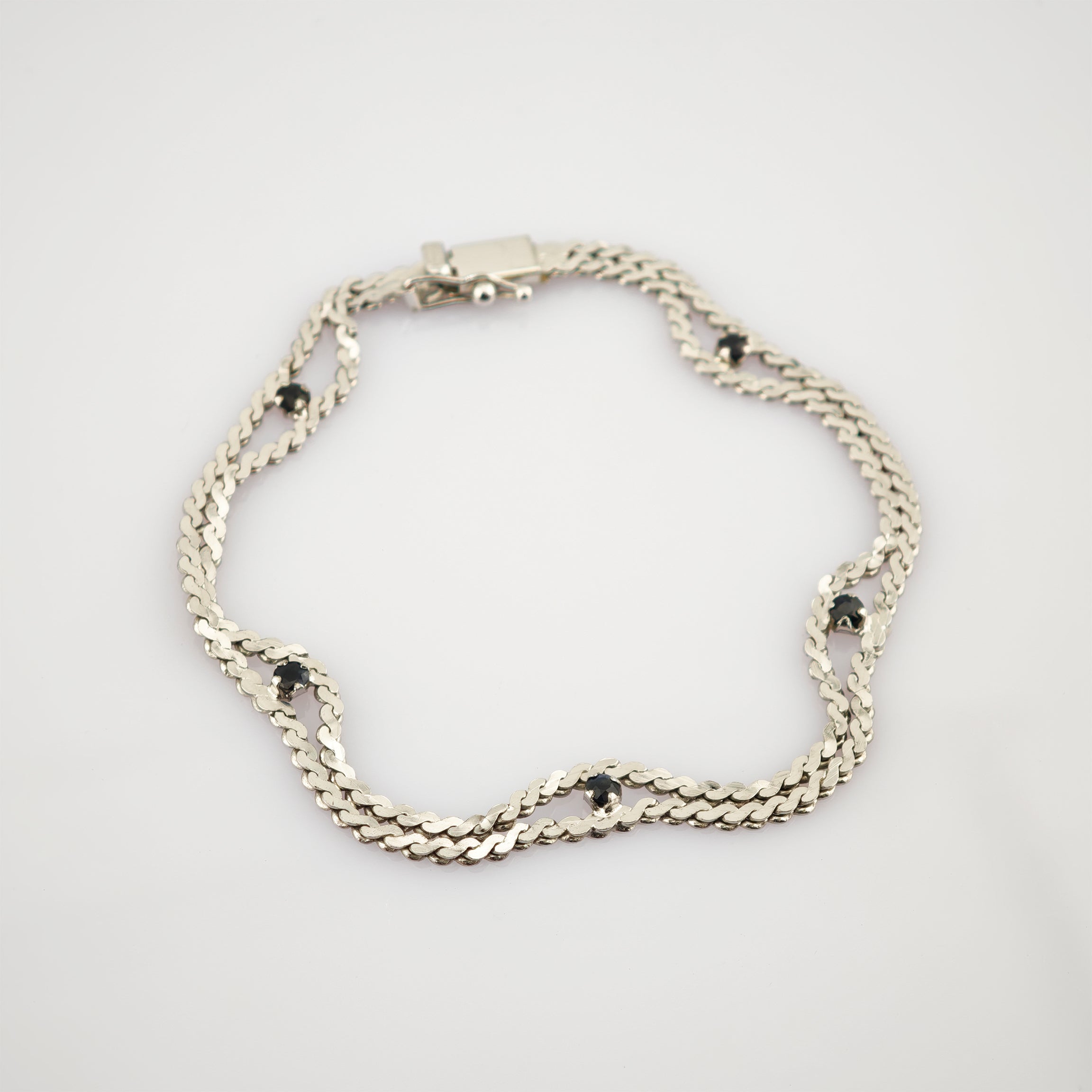Silbernes Armband mit doppelter Kettenoptik und kleinen schwarzen runden Edelsteinen auf weißem Hintergrund.