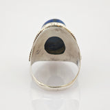 Silberring mit rundem blauem Edelstein und gedrehtem Silberseil-Design auf reflektierender Oberfläche.