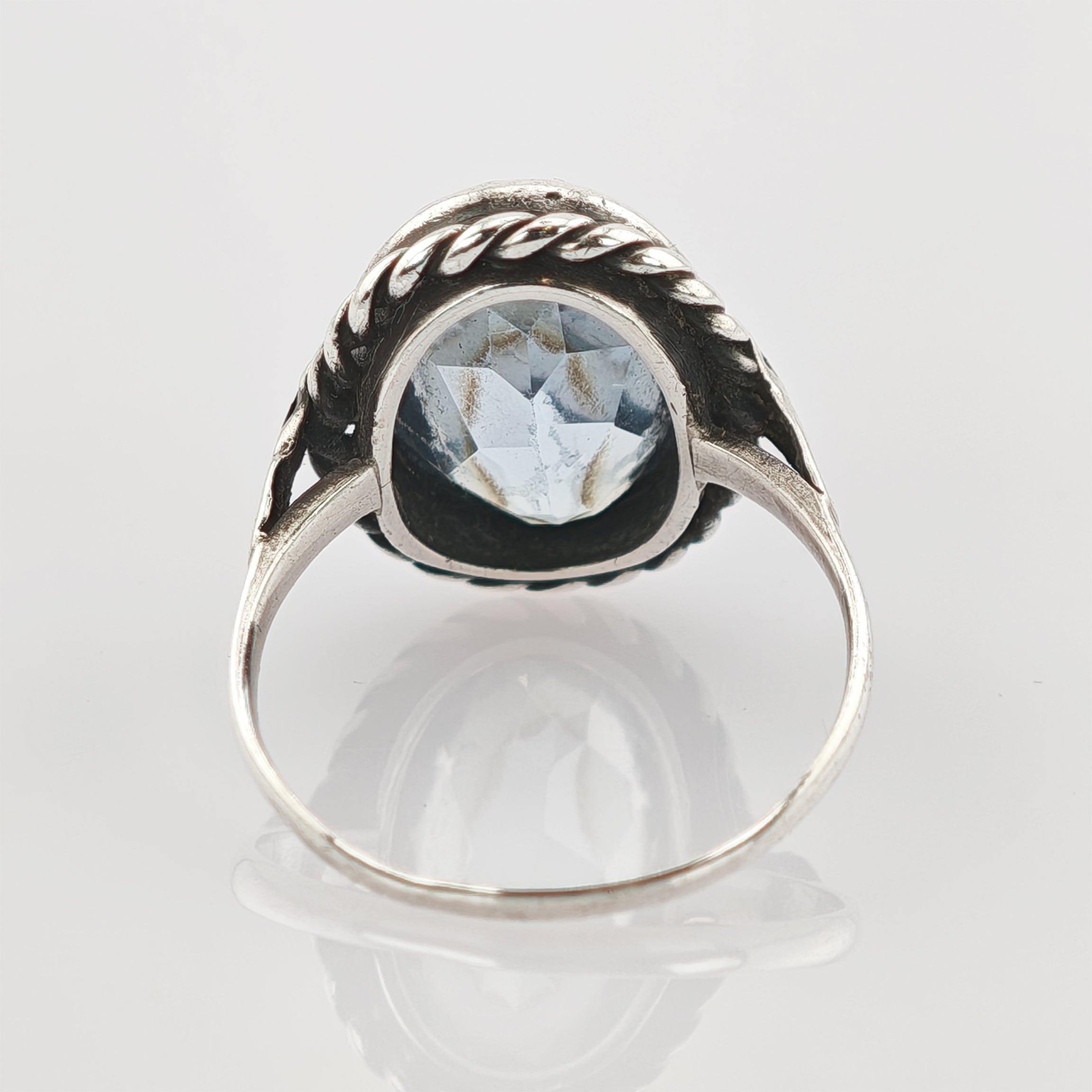 Silberring mit facettiertem blauem Edelstein und Seilrand auf weißer Oberfläche