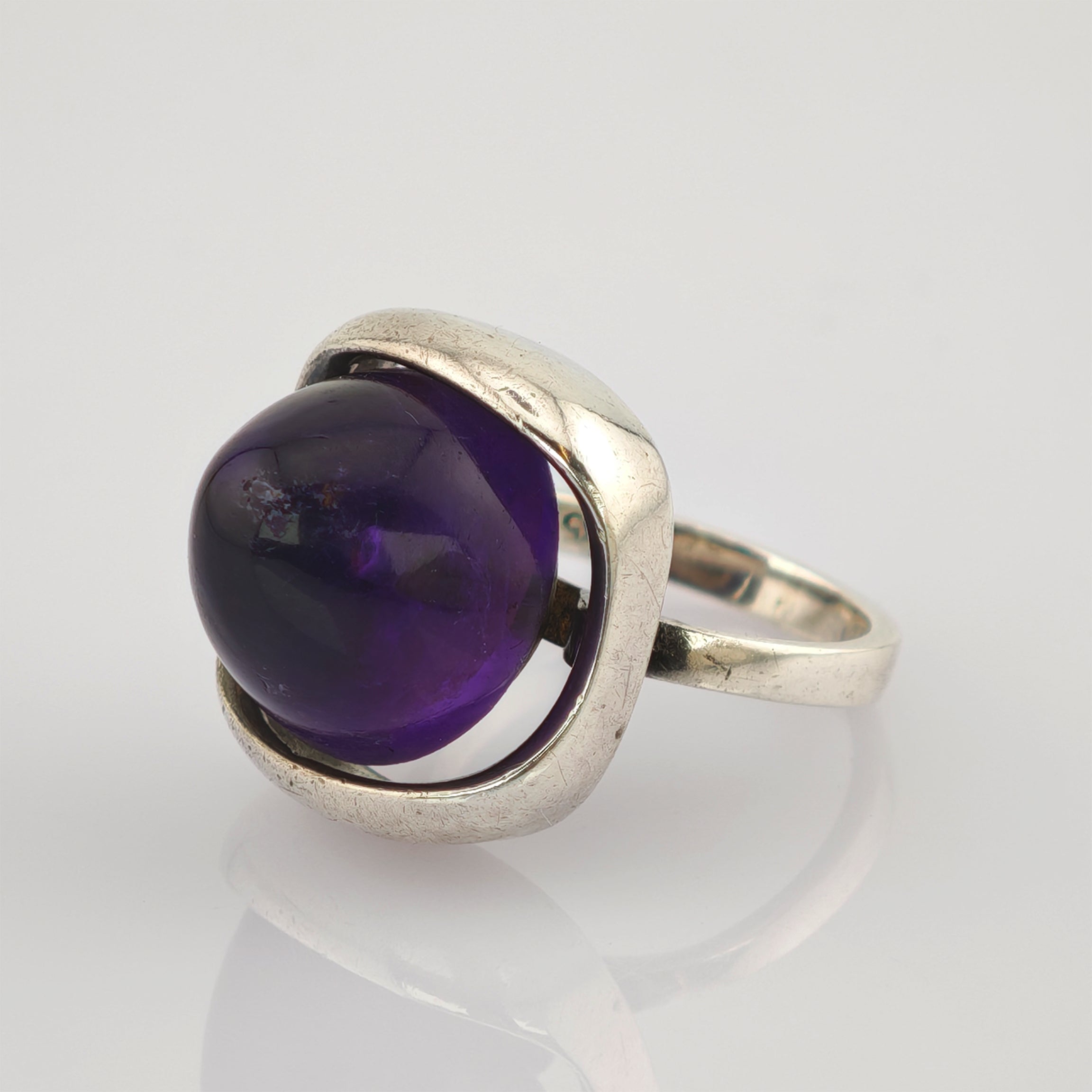 Silberring mit großem, rundem, poliertem Amethyst in offener Fassung auf reflektierender Oberfläche
