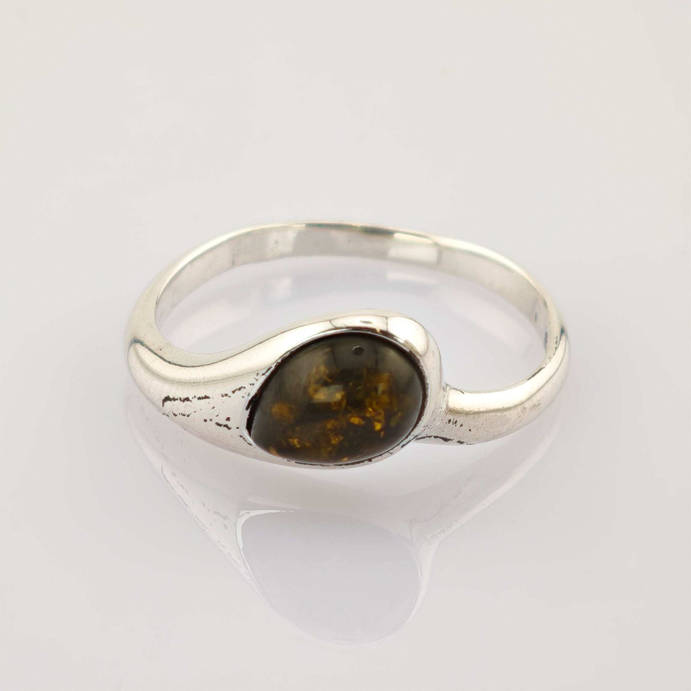 Silberring mit abgerundetem Band und ovalem dunklem Bernstein und goldenen Einschlüssen auf reflektierender Oberfläche.