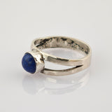 Silberring mit tiefblauem, rundem Stein und geteilter Ringschiene auf weißem Hintergrund.