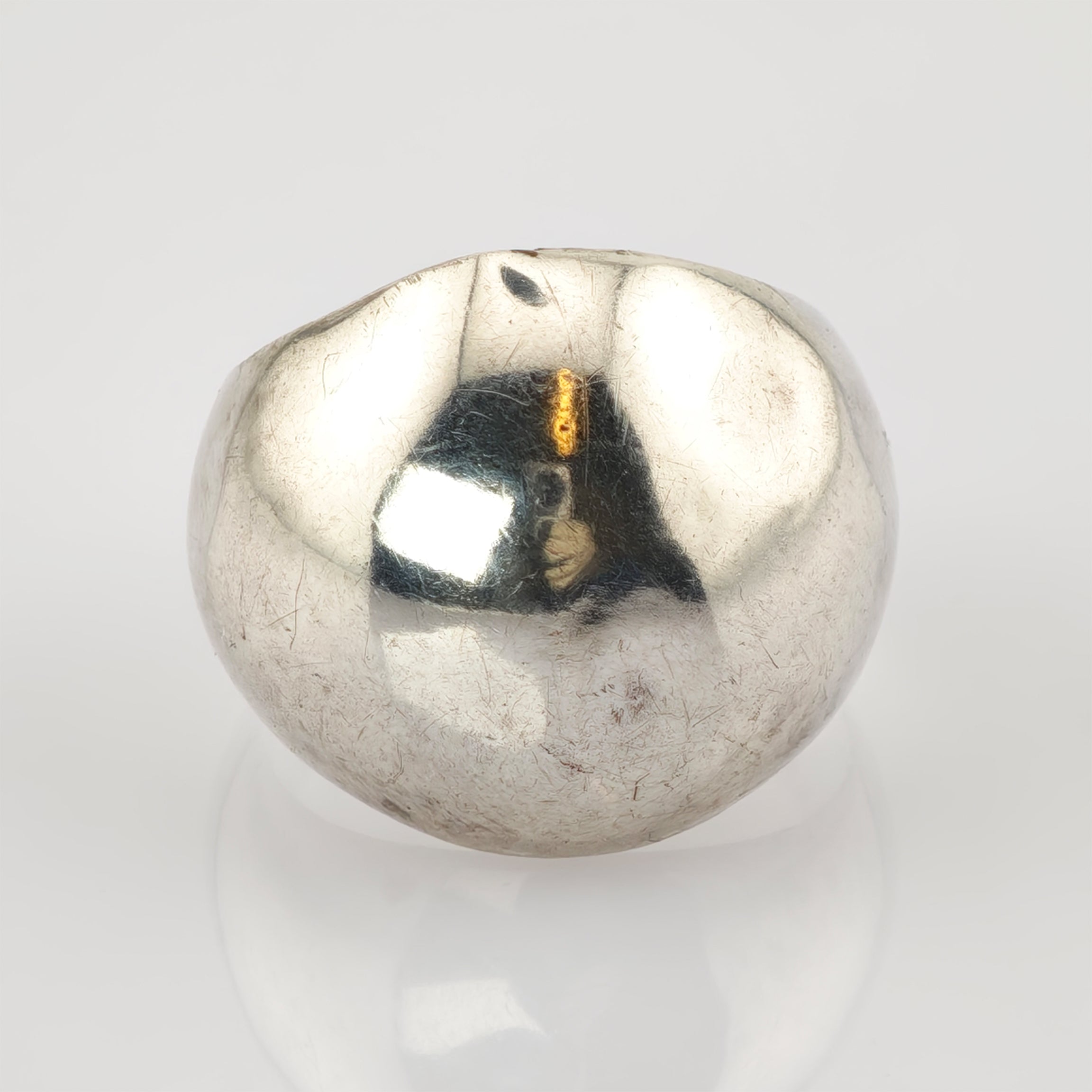 Unregelmäßig geformtes silbernes Metallstück mit reflektierender und leicht zerkratzter Oberfläche vor weißem Hintergrund.