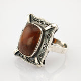 Rechteckiger Vintage-Ring mit poliertem braunem Bernstein und silbernem Rahmen mit Wirbelmustern.