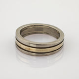 Zweiseitiger Metallring mit silbernem Außenband und goldenem Innenband auf reflektierender Oberfläche